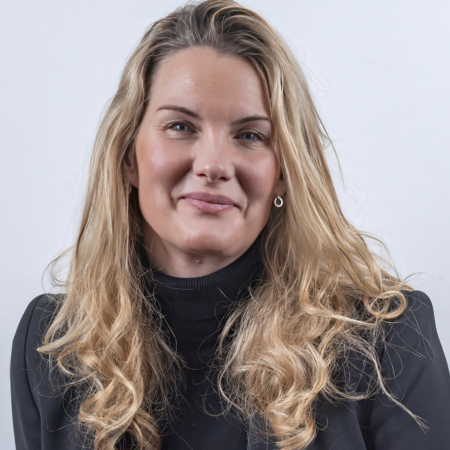 Kvinna med långt, blont hår och svart polotröja står mot en vit bakgrund och ler lätt.