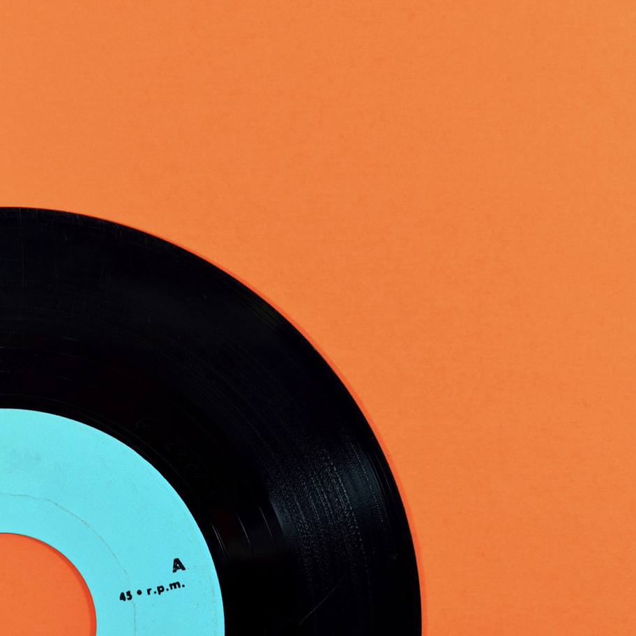 Närbild av en svart vinylskiva med en turkos etikett, delvis synlig mot en stark orange bakgrund. Etiketten visar texten "45 r.p.m.", vilket indikerar att det är en singelskiva.