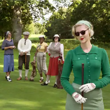En kvinna i en grön vintagekofta, ljusgrön kjol och vita golfhandskar står i förgrunden på en golfbana, lutad mot sin klubba. Hon har blont lockigt hår, ett grönt prickigt hårband och solglasögon, och hon bär rött läppstift. Bakom henne syns en grupp på fyra personer i retroinspirerade golfkläder från tidigt 1900-tal. De bär tidstypiska hattar, västar, knälånga kjolar och golfbyxor, och håller golfklubbor och väskor. Bakgrunden består av en grön golfbana omgiven av stora träd, och stämningen är elegant och nostalgisk.