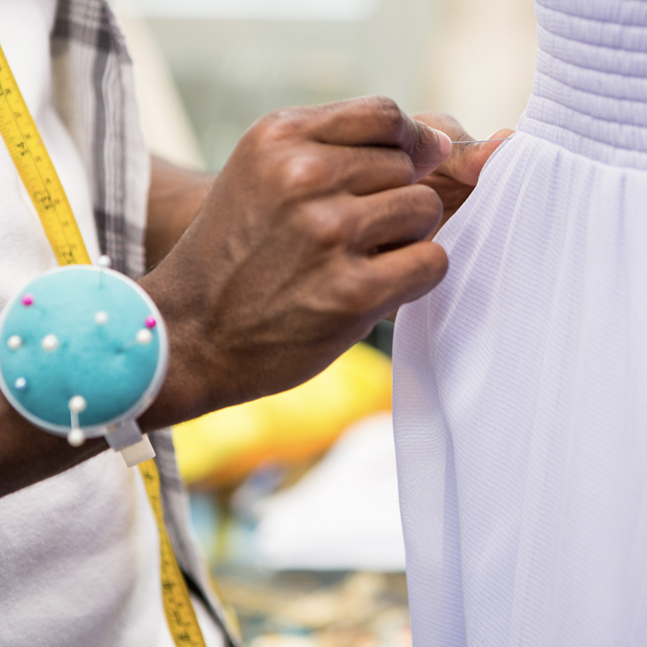 Närbild på en persons händer som nålar en klänning. 