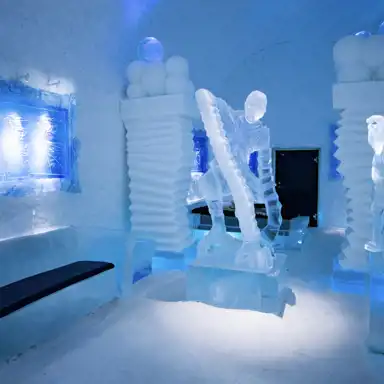 Ett unikt isrum med en stor isskulptur av hockeyspelaren Börje Salming i en offensiv position, med en ishockeyklubba i handen. Skulpturen står på ett upphöjt isblock, vilket ger en känsla av rörelse och dynamik. Rummet är upplyst med blått och vitt ljus, vilket förstärker den frostiga atmosfären. På väggarna syns lysande blå konstverk inramade i is, och de robusta pelarna är dekorerade med runda isklot på toppen. Svarta dynor på isbänkar ger en kontrasterande touch till den annars genomskinliga miljön.