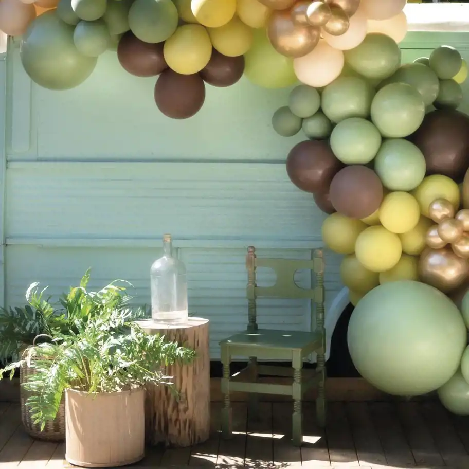 Arkad av gula, gröna och bruna ballonger, hänger ovanför en grön stol utomhus. 