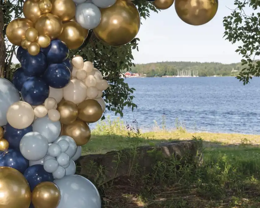 Arkad av blå och guldfärgade ballonger med strand och vatten i bakgrunden.  