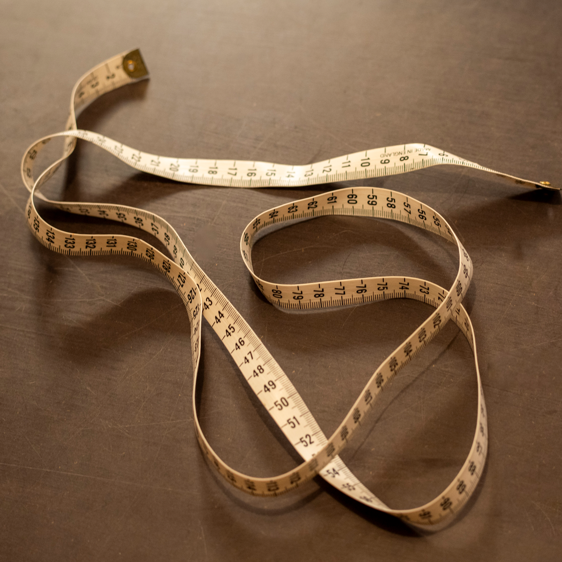 Ett måttband ligger i mjuka slingor på en mörk bordsyta. Måttbandet är ljust med tydliga siffror och markeringar.