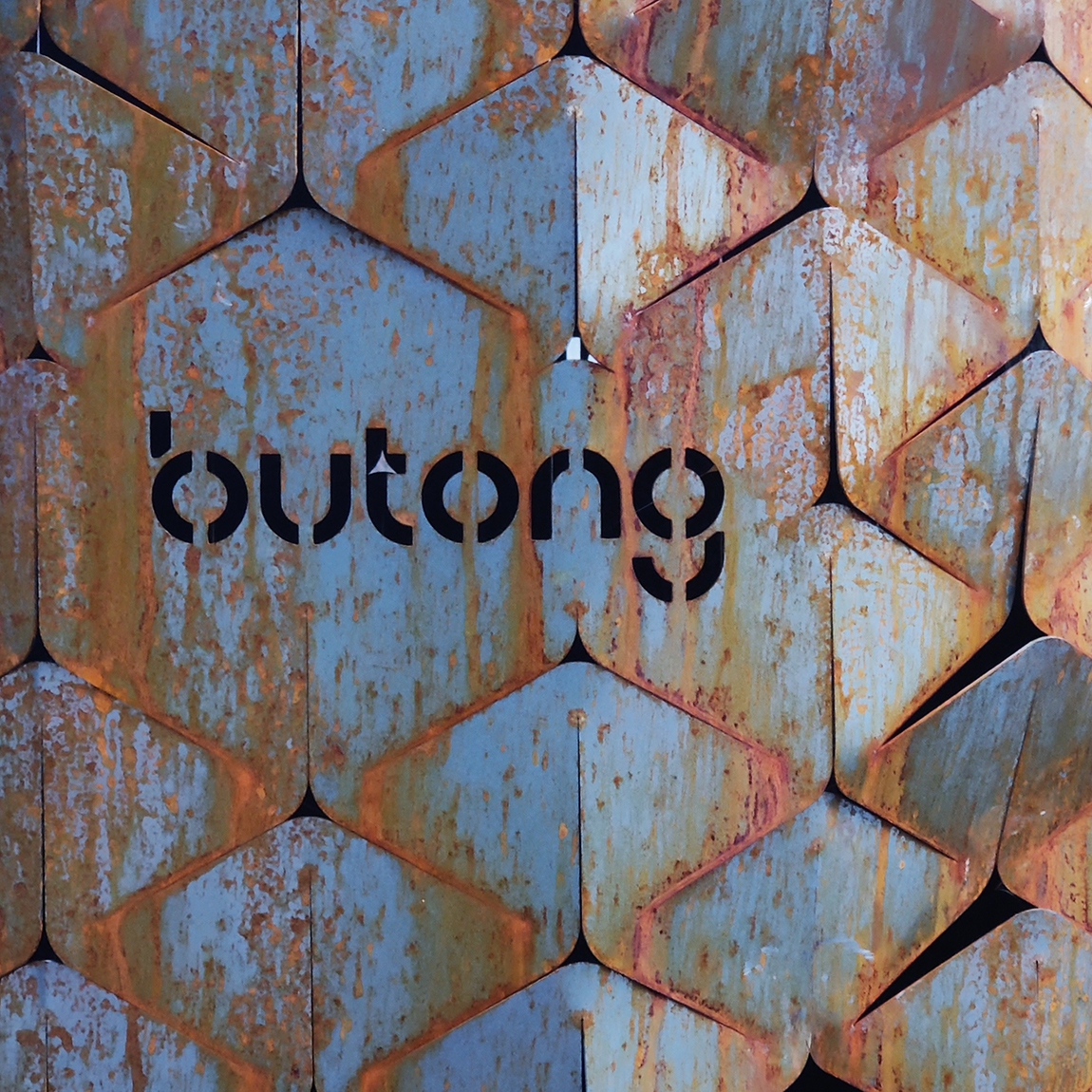 Närbild av Butongs fasettformade metallpaneler med rostig yta och utskuren logotyp i svart.