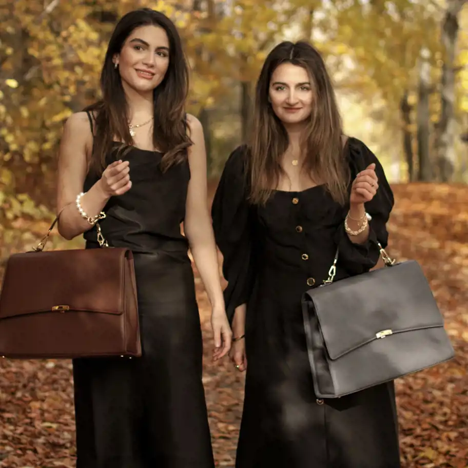 Systrarna Persheng och Perdica Babaheidari på en stig i skogen med en brun och en grå handväska.  