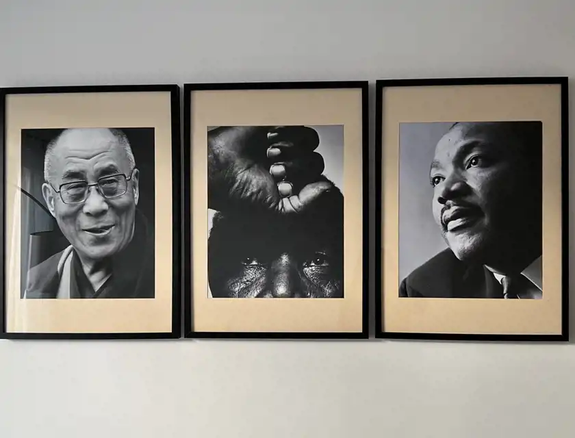 Tre inramade svartvita porträtt hänger på en vit vägg. Från vänster till höger visar bilderna en leende Dalai Lama med glasögon och en traditionell klädsel , mittenpersonen är Nelson Mandela vars ögon syns under en upphöjd knuten näve, och den tredje är Martin Luther King i kostym som blickar uppåt. Bilderna är estetiskt sammanhängande med svarta ramar och en ljus passepartout.