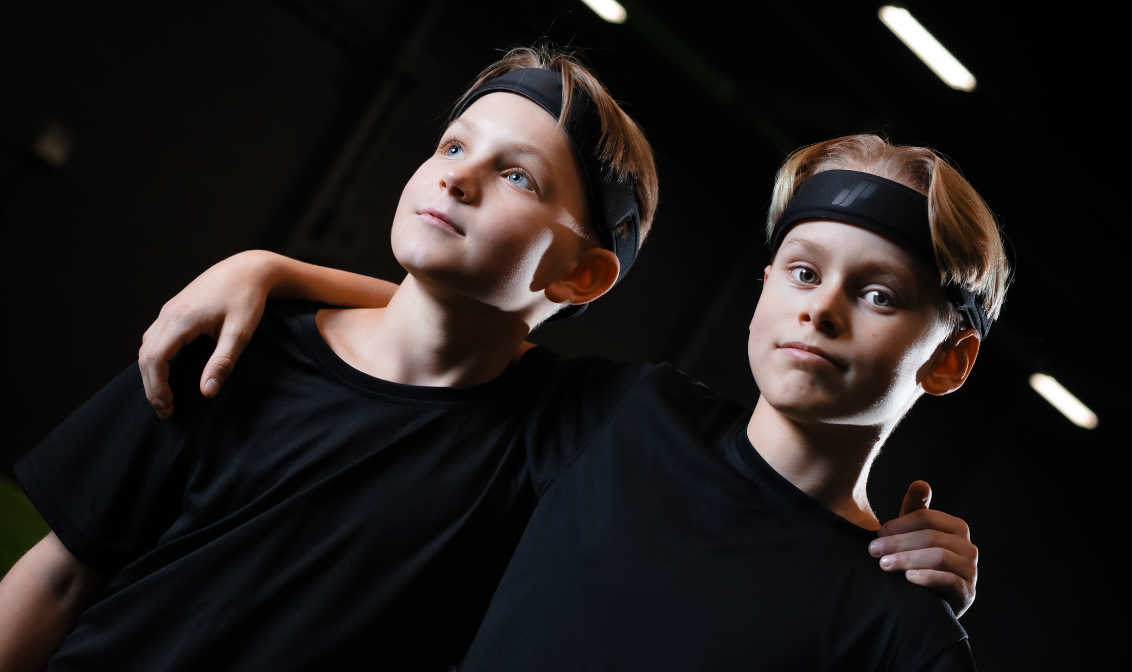 Två unga fotbollsspelare bär huvudskydd från DAJE Prevent och står tillsammans på en fotbollsplan.