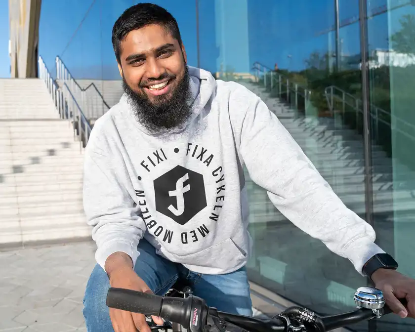Rafi Mohammad sitter på en cykel och tittar in i kameran och ler. 