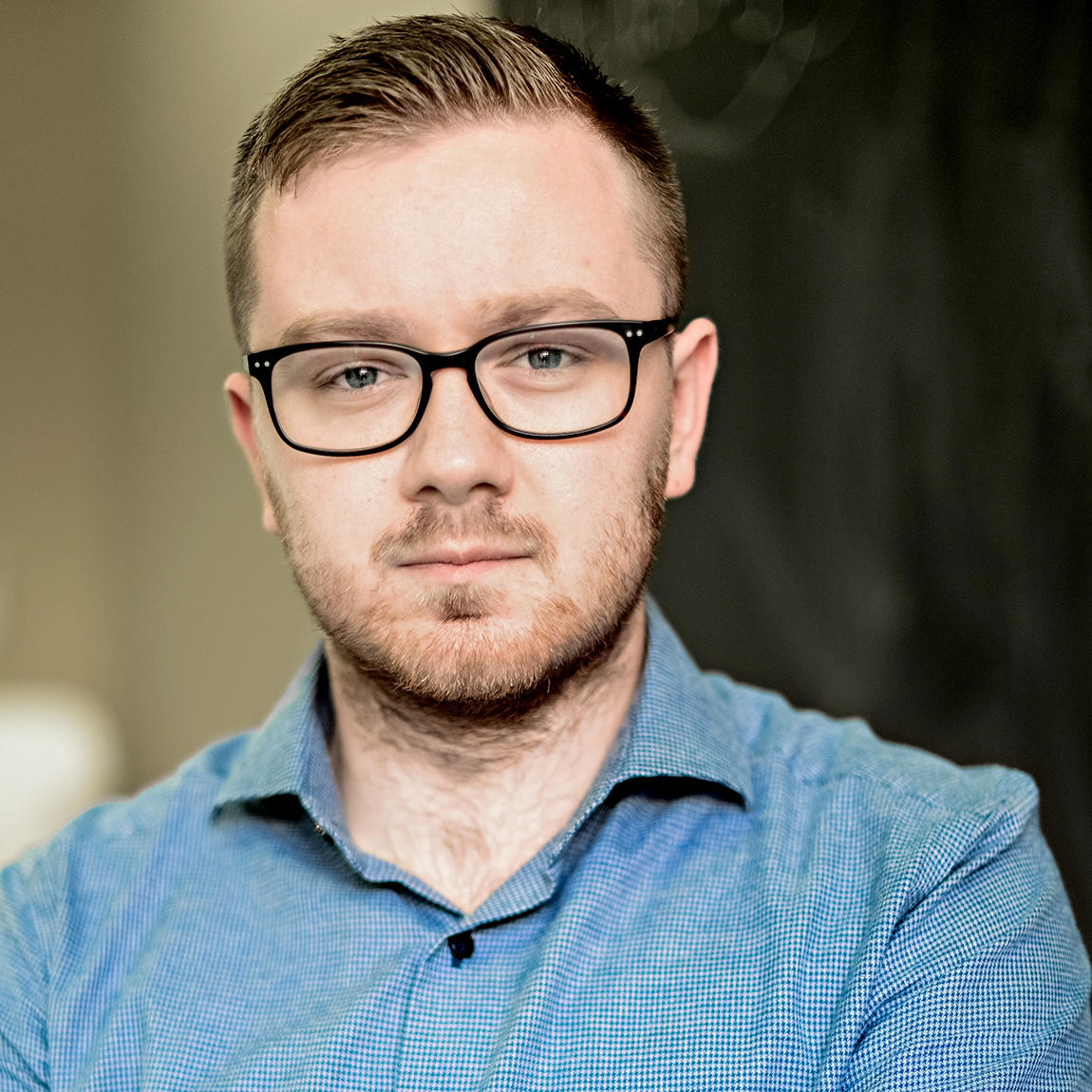 Grundaren av Guestro porträtterad inomhus, med glasögon och skjorta, mot en mörk bakgrund.