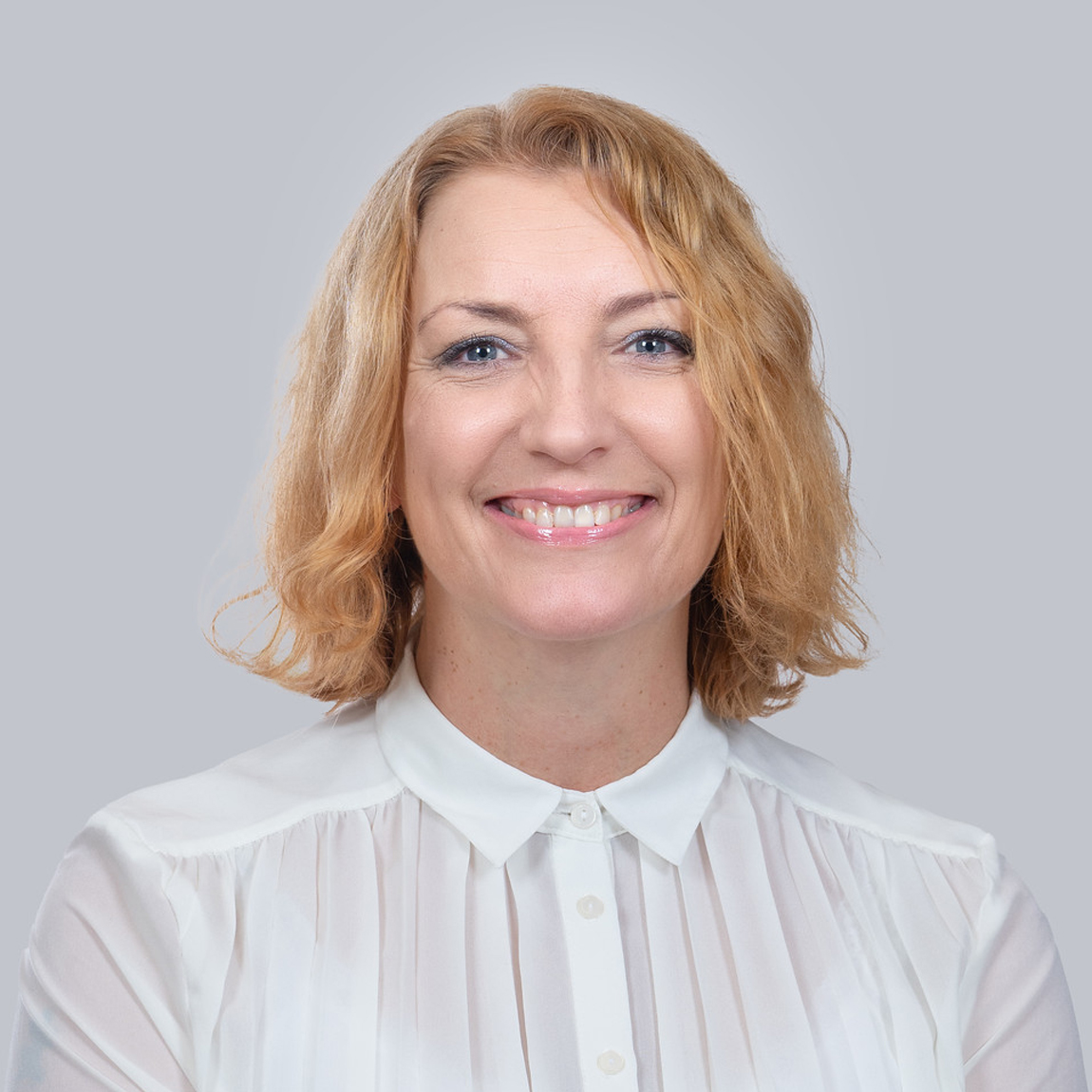 Ellinor Mellgren, rådgivare hos Almi, ler mot kameran. Hon har axellångt blont hår, bär en vit blus med ståkrage och sitter mot en ljusgrå bakgrund. Bilden ger ett professionellt och varmt intryck.