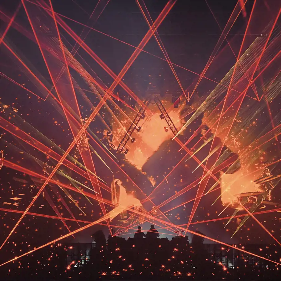 En scen med en spektakulär ljusshow där röda och gula laserstrålar korsar varandra i olika riktningar. I bakgrunden syns en stor skärm med eld- och rökanimationer. Silhuetterna av två personer, troligen DJ:s, står vid ett upphöjt podium, omgivna av en stämningsfull och intensiv visuell effekt.