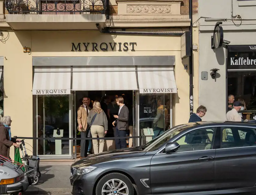 Folk samlas utanför Myrqvists butik, med randiga markiser och skyltfönster som visar eleganta skor.