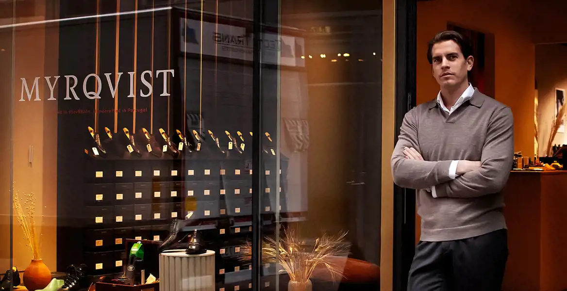 Sebastian Öhrn, vd och grundare av Myrqvist, står utanför butikens skyltfönster där eleganta skor visas upp på hyllor.