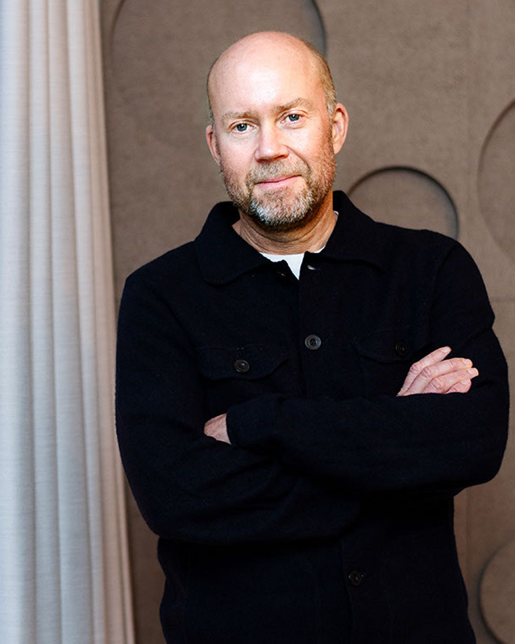 Porträtt av ägaren till Odyssey som står inomhus med armarna i kors framför en vägg med runda former.