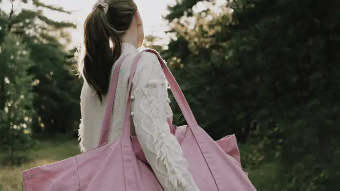 Kvinna bakifrån med rosa tygkasse i motljus.