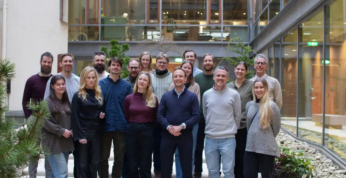 En grupp på cirka 20 personer står tillsammans i en ljus, modern inomhusgård och ler mot kameran. Bilden signalerar samarbete, innovation och laganda.