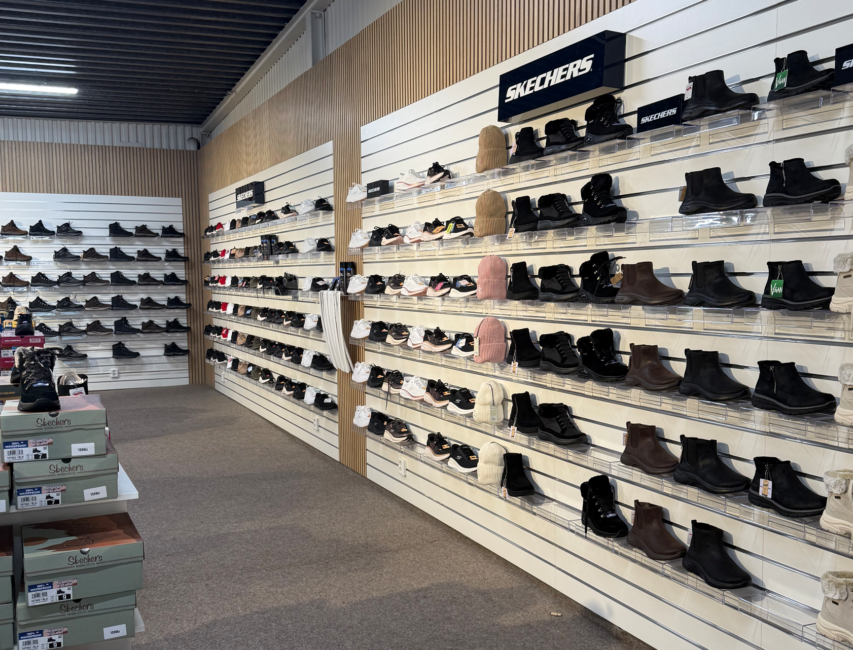 Skohylla i Ronneby Outlet med ett brett utbud av skor uppställda längs väggarna. Ljus och rymlig butiksmiljö med tydlig varuexponering.