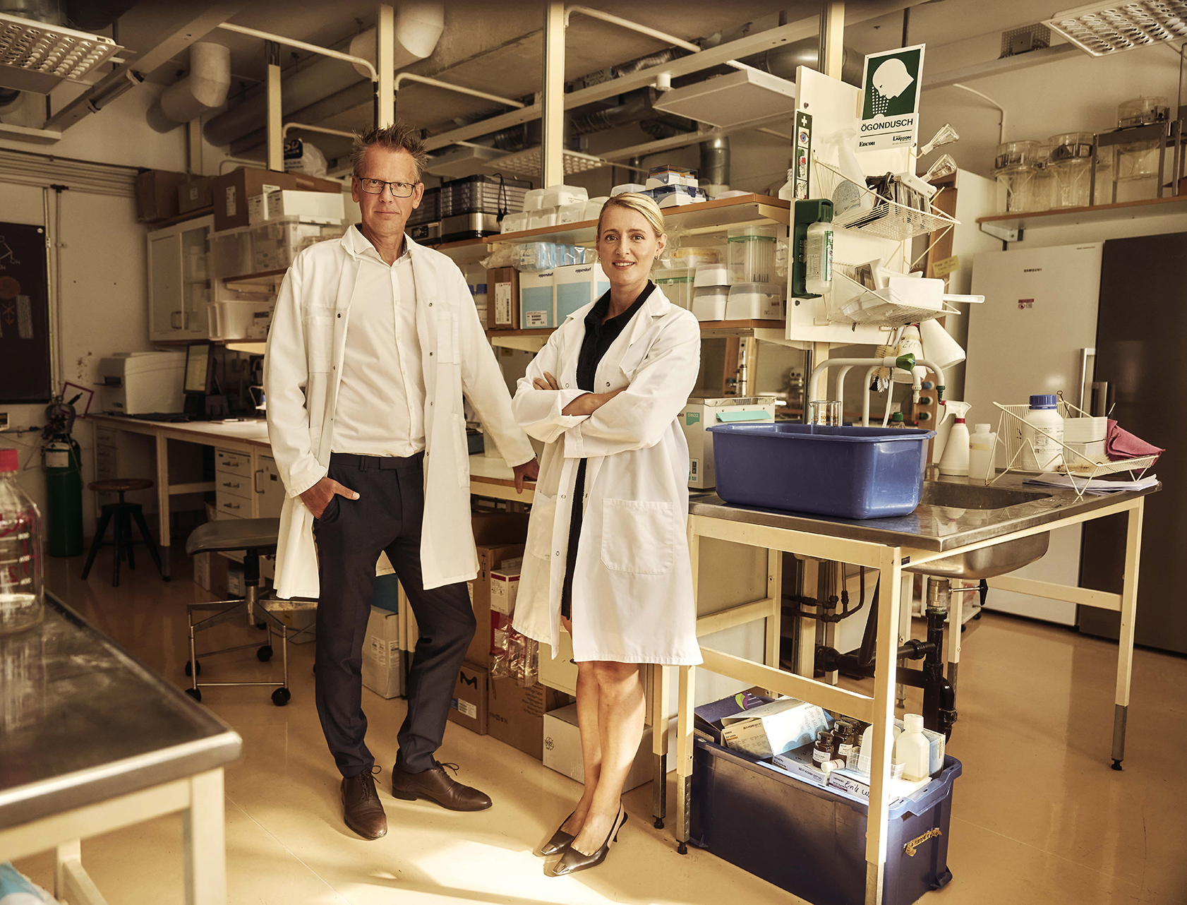 Två medgrundare av Sigrid Therapeutics står i ett laboratorium, klädda i vita labbrockar bland bänkar och laboratorieutrustning.