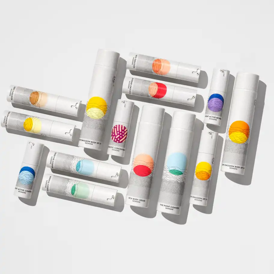 Ett urval av Skinomes hudvårdsprodukter med färgglada etiketter i olika nyanser, liggande på ett vitt underlag i ett mönster.