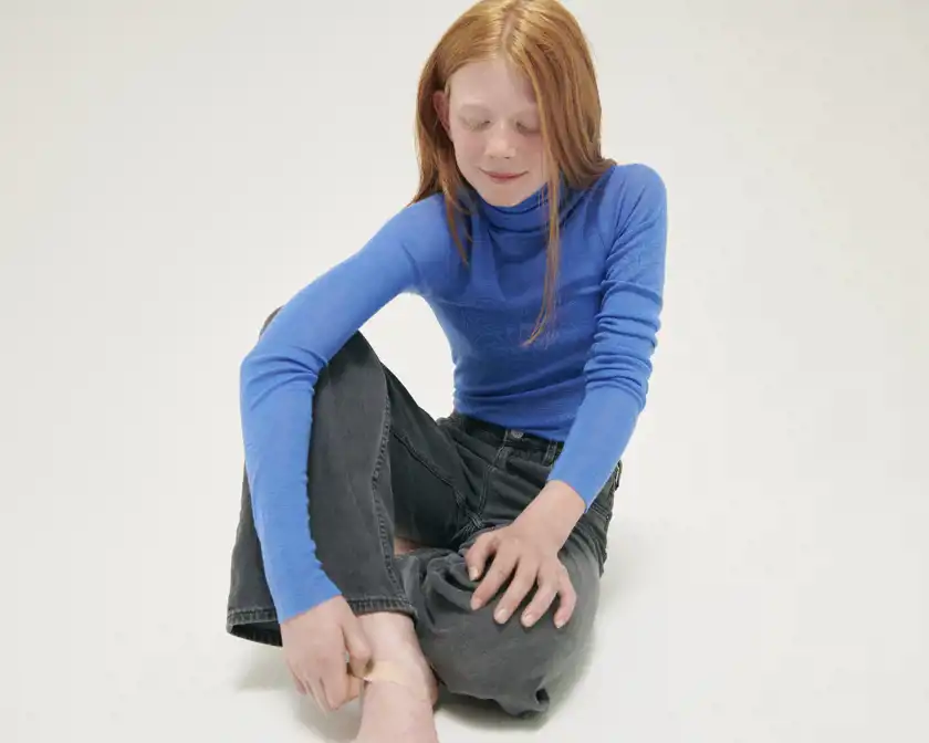 Flicka sitter på golvet och sätter på ett plåster på sin fot.