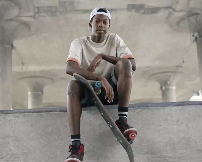 Pojke med plåster på sitt knä sitter på en bänk med sin skateboard.