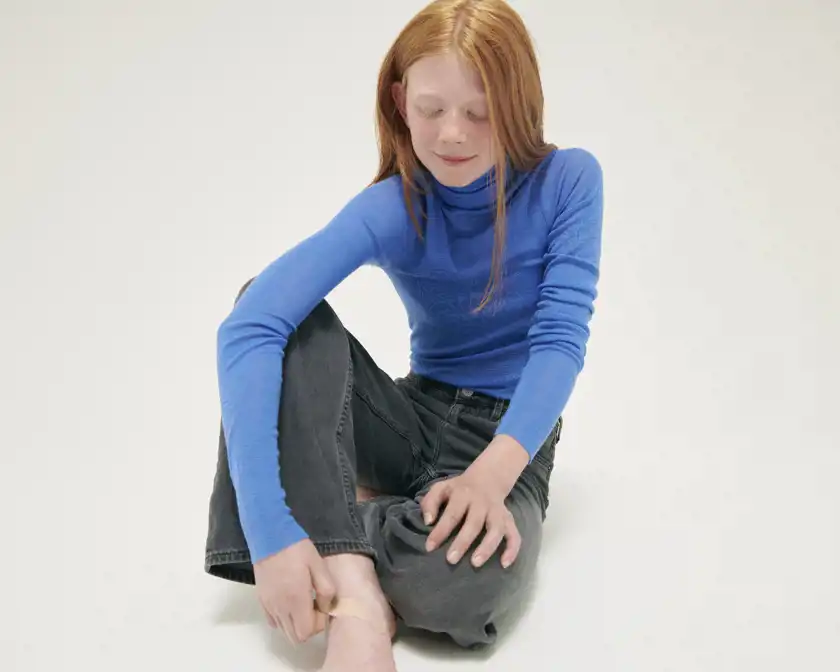Flicka sitter på golvet och sätter på ett plåster på sin fot. 