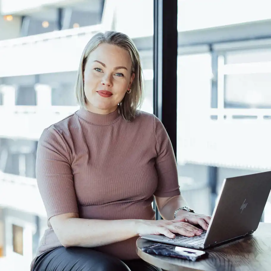 Jenni Laapotti sitter med sin laptop och tittar in i kameran. 