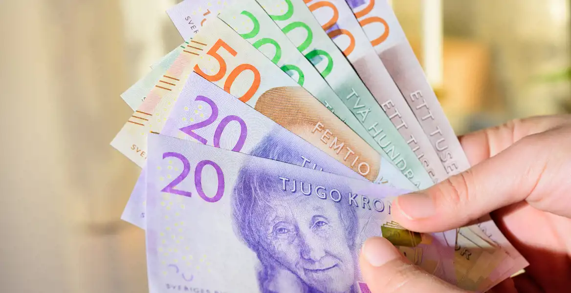 Närbild på en hand som håller i svenska sedlar. 