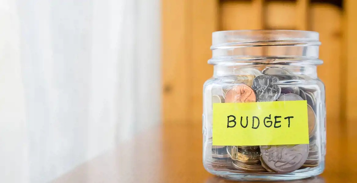Närbild på en glasburk med mynt, och som har en postit-lapp märkt med budget.