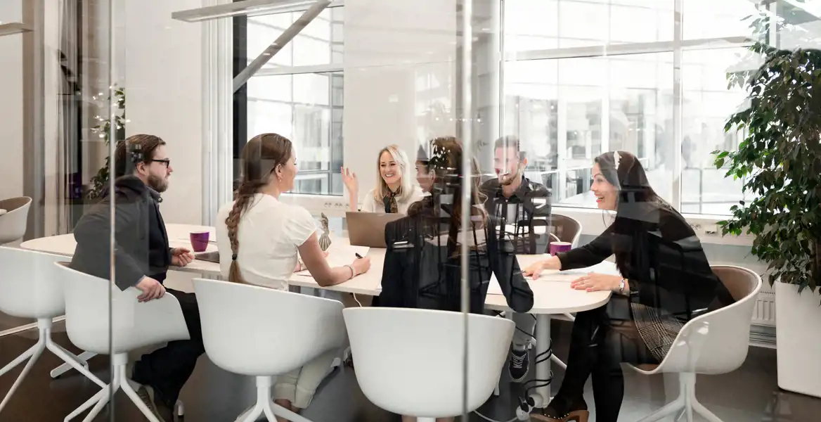 En grupp människor sitter i möte bakom en glasvägg.