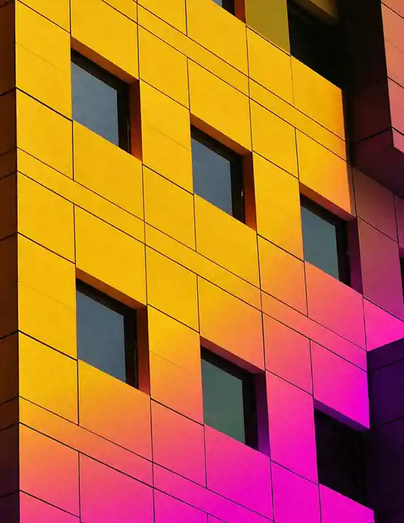 En modern byggnadsfasad med geometriskt mönster av fyrkantiga fönster, där den gula ytan övergår i rosa och lila nyanser genom en ljusreflektion eller färgeffekt, vilket skapar ett dynamiskt och konstnärligt uttryck.