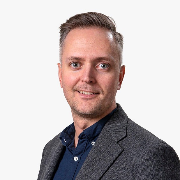 Man med kort grått hår, klädd i en mörkgrå kavaj och mörkblå skjorta, ler och ser in i kameran mot en neutral grå bakgrund. Fredric Genberg är vd på ett av Almis dotterbolag, Almi Nord.