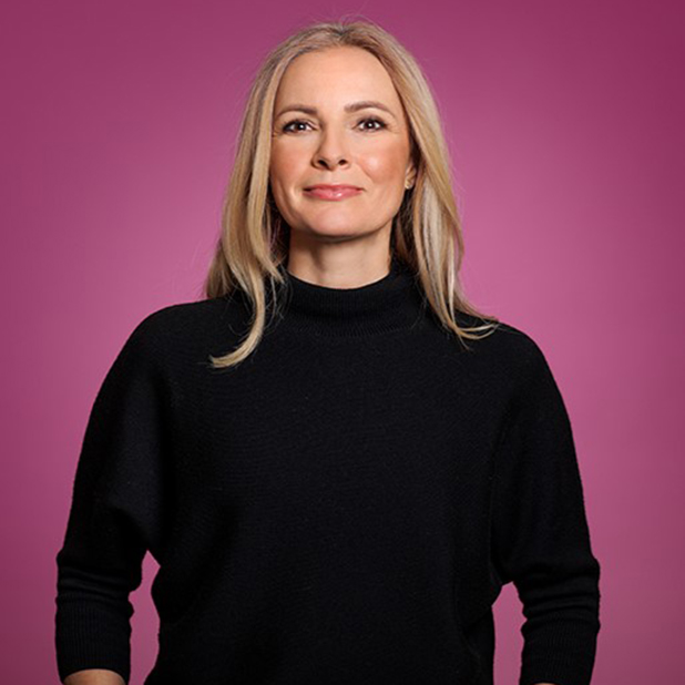 Kvinna med långt blont hår och svart polotröja, ler mot kameran med en rosa bakgrund. Natasa Pahlm jobbar som Investment Manager på Almis dotterbolag Almi Invest.