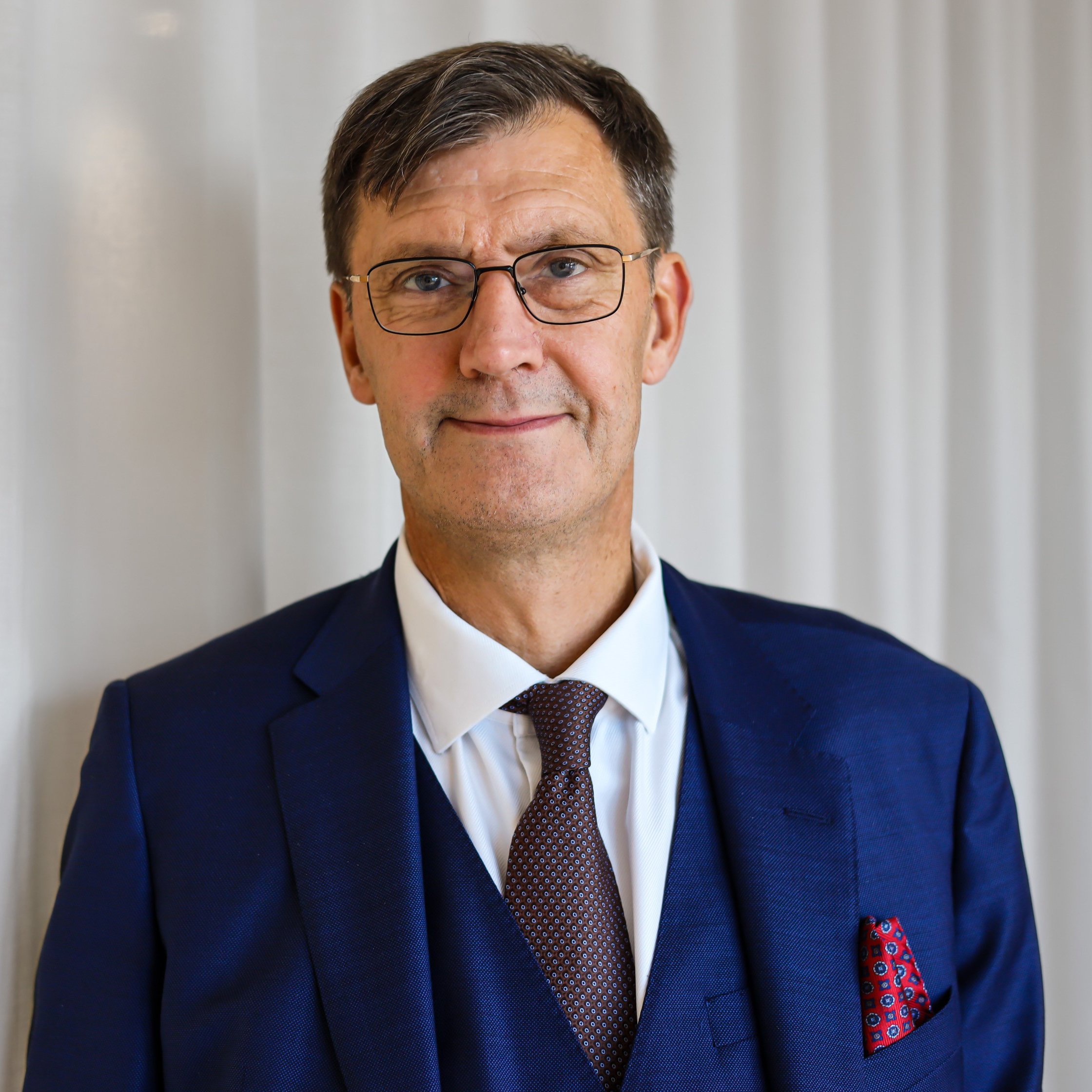 Porträttbild av en man i kostym, slips och glasögon. Bakgrunden är ljus och neutral, vilket ger en ren och elegant framtoning. Han har en självsäker och vänlig uppsyn, vilket gör att bilden passar bra för affärssammanhang eller professionella presentationer. Jan Arpi, CFO Almi AB.