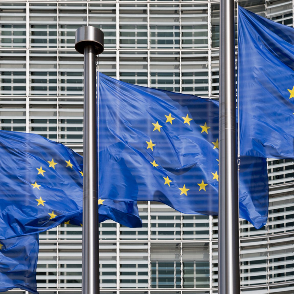 EU-flaggor vajar framför en modern byggnad. Bilden symboliserar EU:s arbete med hållbarhetsfrågor och den gemensamma taxonomi som styr vilka investeringar som klassas som miljömässigt hållbara.