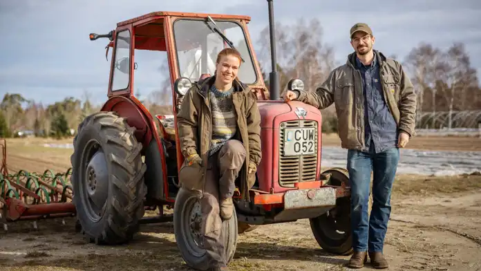 Elin och Einar Hoas står lutade mot en röd traktor framför en åker på gården Lilla Bjers.