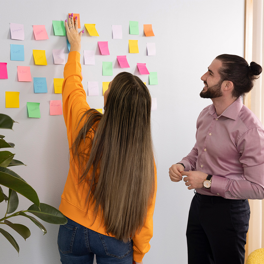 två personer vid en whiteboard full med post-it lappar
