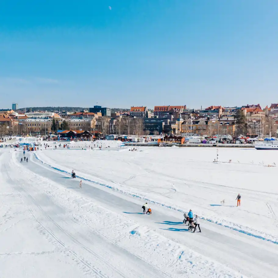 Folk promenerar på isvägen över Storsjön mellan Frösön och Östersund och njuter i solens glans.