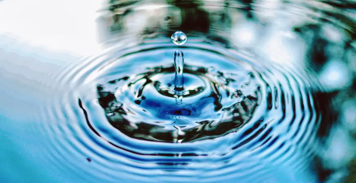 Närbild på ett vattendropp i ett stilla blått vatten med ringar som sprider sig utåt. Bilden symboliserar de effekter och insikter som kan uppstå genom en noggrann due diligence-process inför investeringar eller företagsköp.