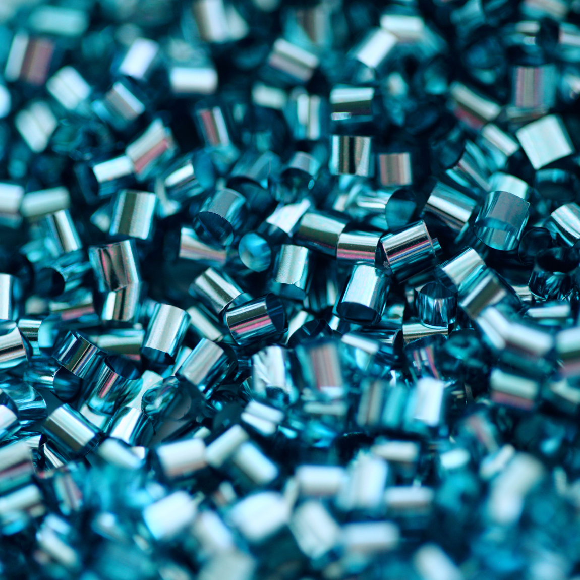Närbild av blanka, blåskimrande plast- eller metallpellets som ligger i en hög.