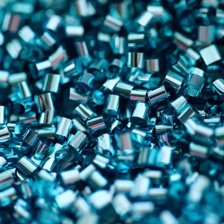Närbild av blanka, blåskimrande plast- eller metallpellets som ligger i en hög.
