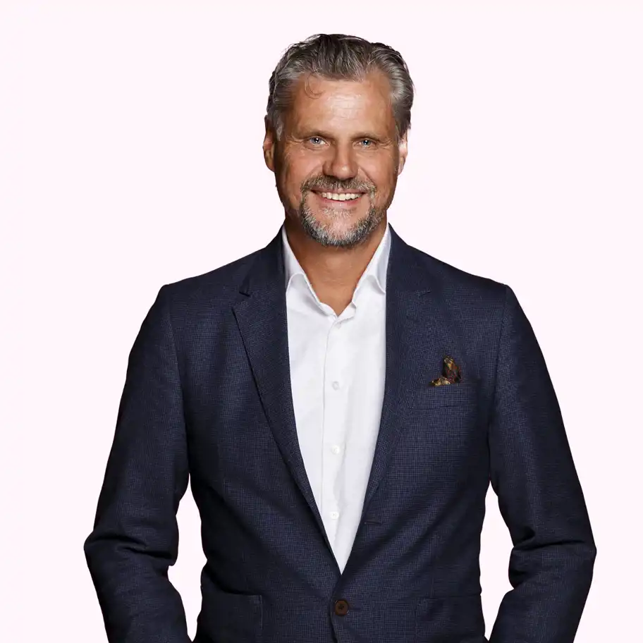 Boris Gyllhamn, Investment Manager på Almi Invest Stockholm, står leende i mörkblå kavaj med vit skjorta och mönstrad näsduk mot en ljusrosa bakgrund.