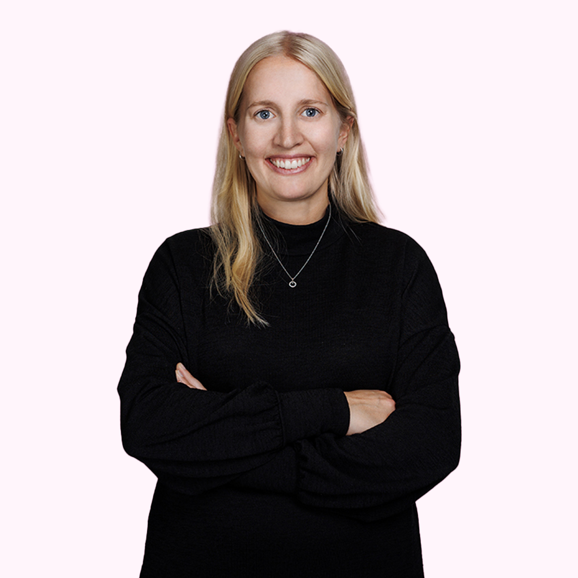 Emma Hanaeus, Investment Analyst på Almi Invest Västsverige, står leende med armarna i kors, klädd i svart tröja mot en ljusrosa bakgrund.