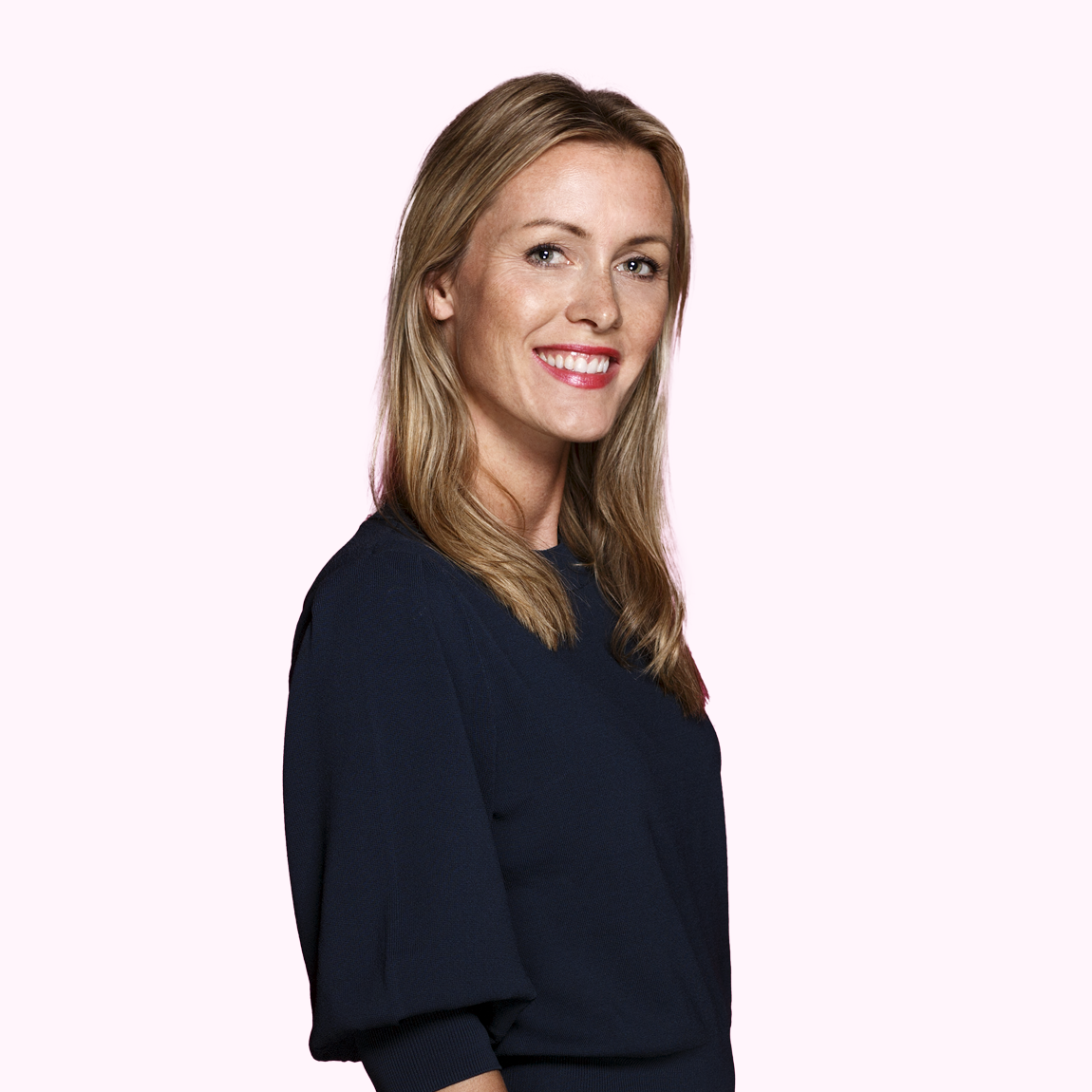 Kajsa Gustafsson, Head of Exits & Portfolio Management på Almi Invest, står leende i mörkblå topp med sidan mot kameran och ljusrosa bakgrund.