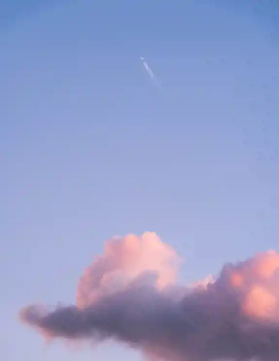 Rosafärgat moln mot en blå himmel och ett flygplan som lyfter i horisonten. 