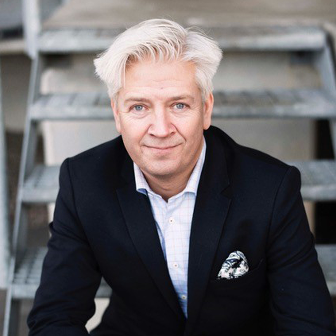 Porträtt av Peter Höjerback, vd för Avidicare. Han bär mörk kavaj, ljus skjorta och mönstrad näsduk. Han sitter i en trappa och ser in i kameran med ett lätt leende.
