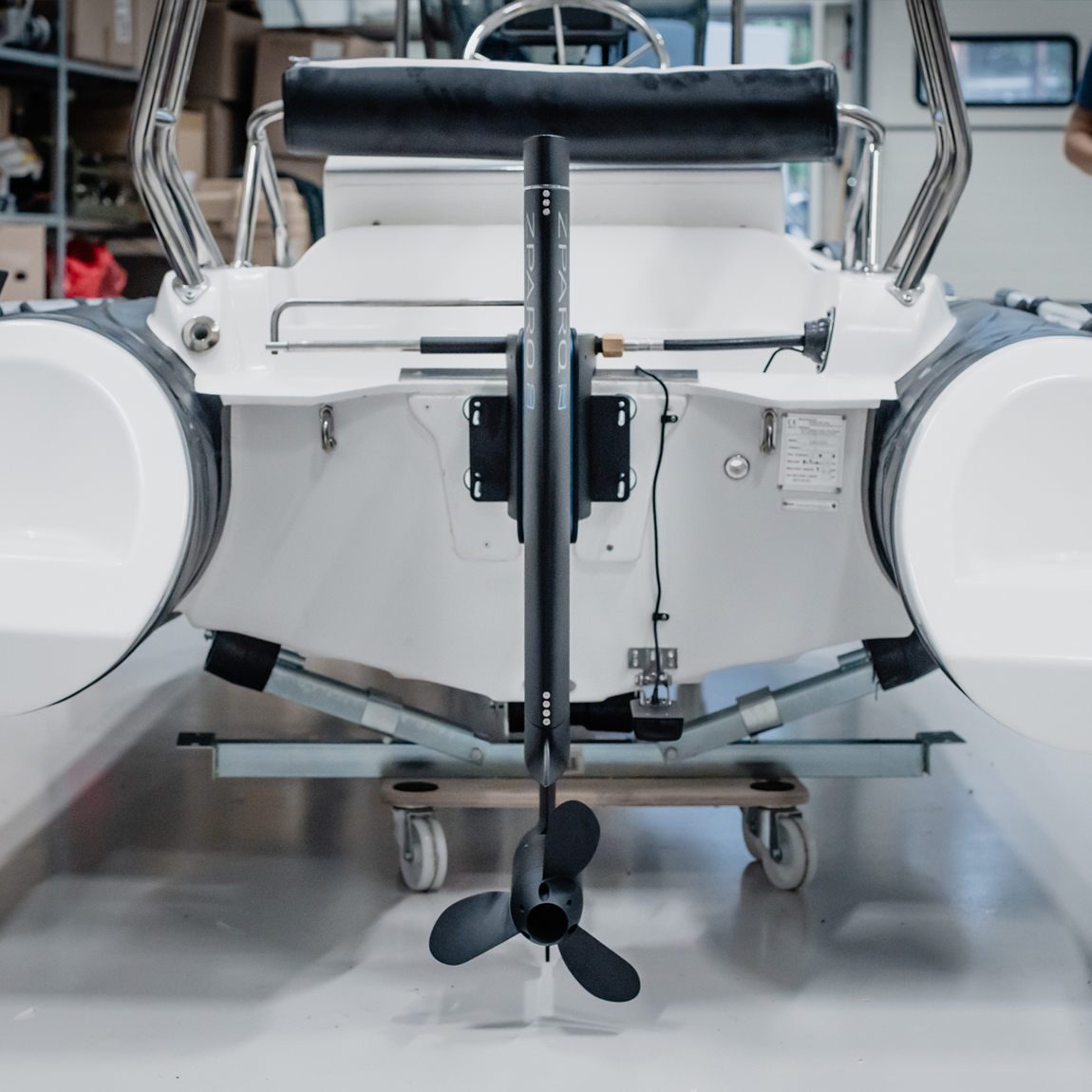 En vit båt står på en vagn i ett garage. På akterspegeln sitter en svart elektrisk utombordsmotor från Zpark, modell Z20, med propeller riktad mot kameran.