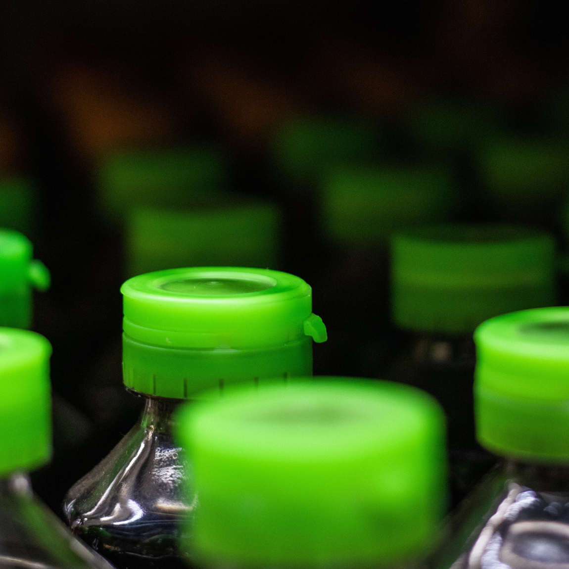 Närbild av plastflaskor med gröna skruvkorkar, uppställda i rader med en oskarp bakgrund.